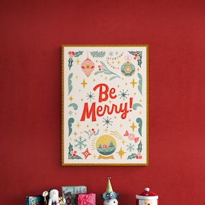 Pu&ograve; includere: Una stampa incorniciata con sfondo bianco e cornice dorata. La stampa presenta un design festivo con un globo di neve, stelle e il testo "Be Merry!" in lettere rosse e bianche.