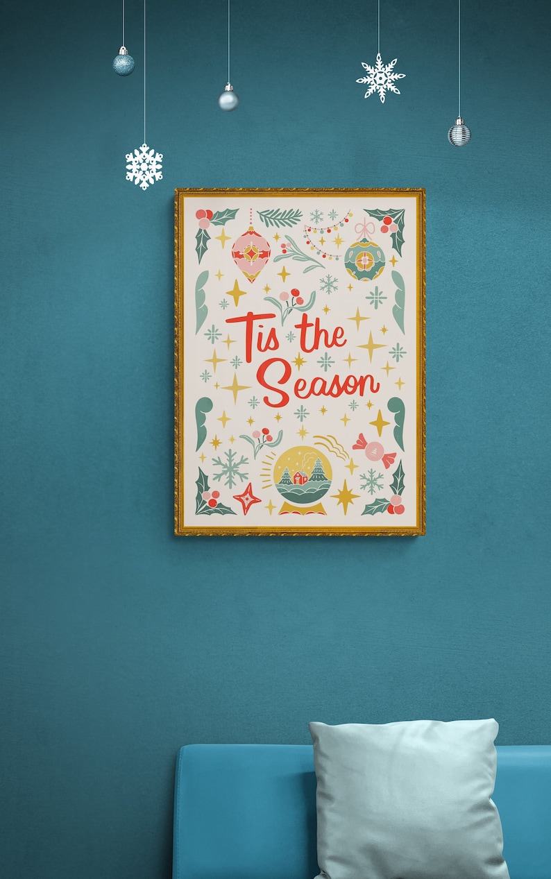 May include: A framed print with a gold frame and a white background. The print features a festive Christmas design with a snow globe, snowflakes, stars, and the text "Tis the Season".