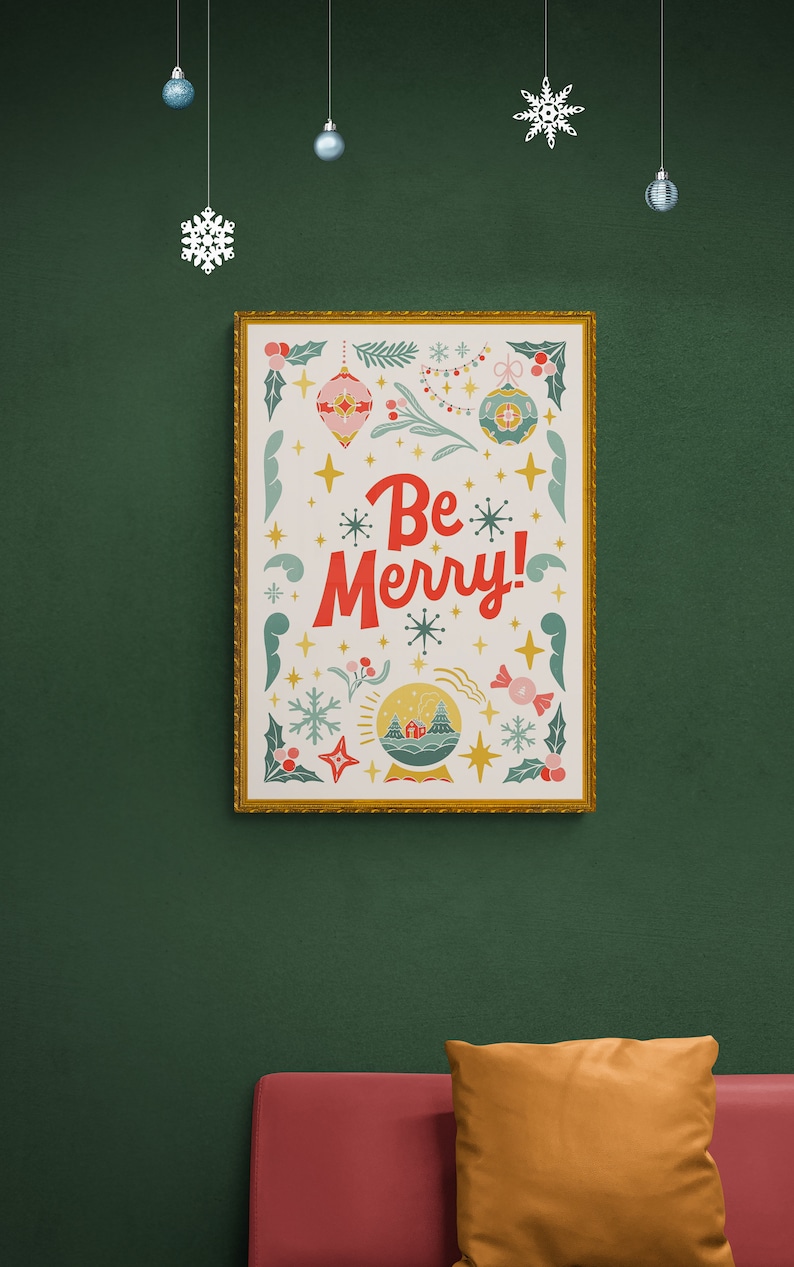 Pu&ograve; includere: Una stampa incorniciata con sfondo bianco e cornice dorata. La stampa presenta un design festivo con una sfera di neve, ornamenti, stelle e il testo "Be Merry!" in rosso.