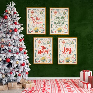 May include: Four framed Christmas prints with festive illustrations and text, including "Tis the Season", "Joy to the World", "Be Merry!" and "Joy", hanging on a green wall with a snowy Christmas tree in the foreground.