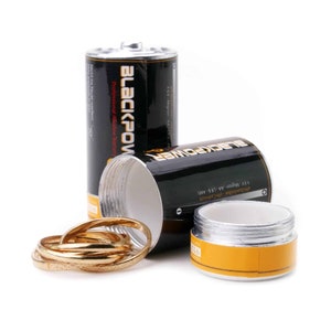 May include: Two black battery-shaped containers with the words "BLACKPOWER" and "Professional Alkaline Battery" printed on them. The containers are open and one contains a stack of gold rings.