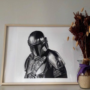 May include: A black and white drawing of a character wearing a helmet and armor, framed in a light wood frame. The drawing is on white paper and is displayed on a white wall.