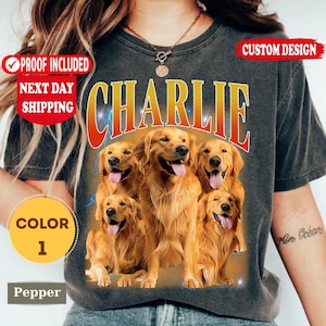 May include: A charcoal gray t-shirt featuring a graphic of four golden retriever dogs with their tongues out. The word CHARLIE is printed in large, bold, orange-to-yellow gradient letters above the dogs. The shirt has a vintage, washed-out look.