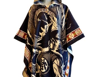 May include: A dark blue hooded poncho featuring a woven graphic of a spiky-haired character and a large dragon. The garment includes two wooden buttons at the neckline, a fringed hem, and decorative borders with circular star patterns and geometric lines.