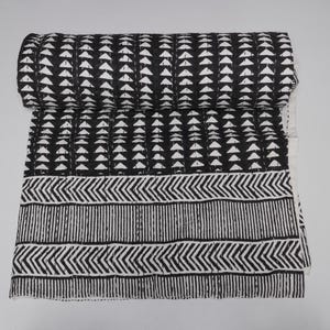 May include: A rolled-up black and white quilt with a geometric pattern. The top section features rows of white triangles on a black background. The bottom section has a border with chevron and vertical stripe designs.