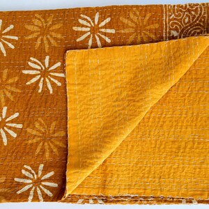 May include: A mustard yellow kantha quilt with a white floral pattern. The quilt is folded in half, showing the plain yellow fabric on the back.