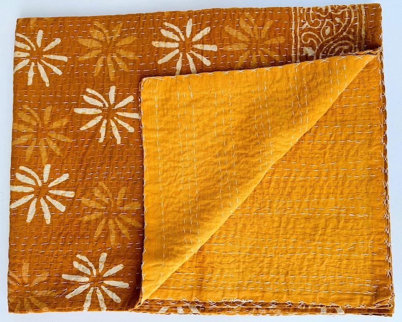 May include: A mustard yellow kantha quilt with a white floral pattern. The quilt is folded in half, showing the plain yellow fabric on the back.