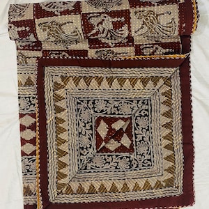 Peut inclure: Une courtepointe en coton pliée présentant un motif en patchwork avec des carrés marron foncé et beige. La section supérieure affiche des figures de danseurs répétitives, tandis que la partie inférieure présente des bordures florales.