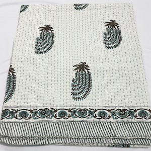 May include: A white cotton quilt featuring a repeating pattern of dark brown and teal paisley-style teardrop motifs. The fabric is detailed with vertical running stitch lines and a decorative border with floral and diagonal striped patterns.