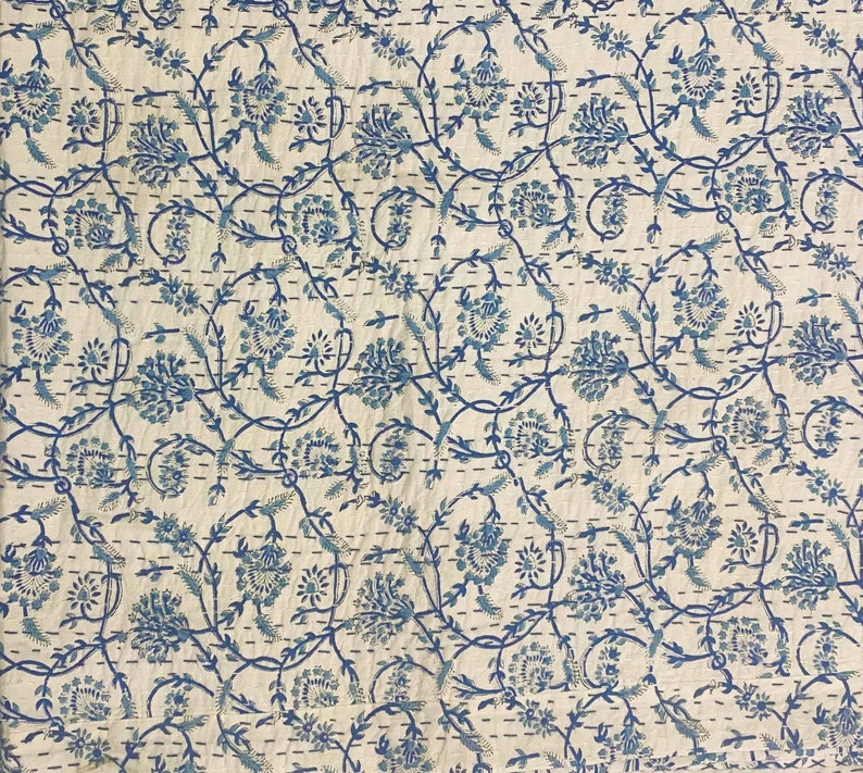 Pode incluir: Um tecido de algod&atilde;o branco com um padr&atilde;o floral azul. O padr&atilde;o apresenta pequenas flores azuis e folhas sobre um fundo branco. O tecido &eacute; acolchoado com um pequeno padr&atilde;o de pontos.