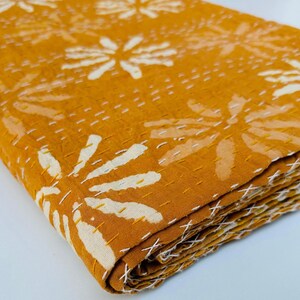 May include: A mustard yellow kantha quilt with a white floral pattern. The quilt is folded in thirds and is made of cotton.