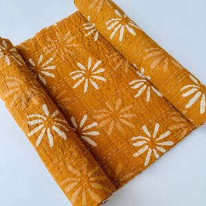 May include: A mustard yellow kantha quilt with a white floral pattern. The quilt is rolled up and ready to be used.