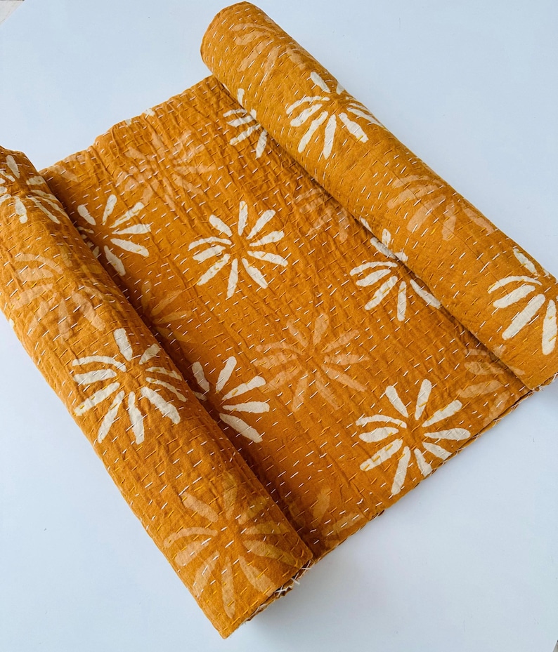 May include: A mustard yellow kantha quilt with a white floral pattern. The quilt is rolled up and ready to be used.