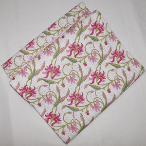 May include: A white cotton quilt with a pink and green floral pattern. The quilt is folded in half and has a subtle sheen.