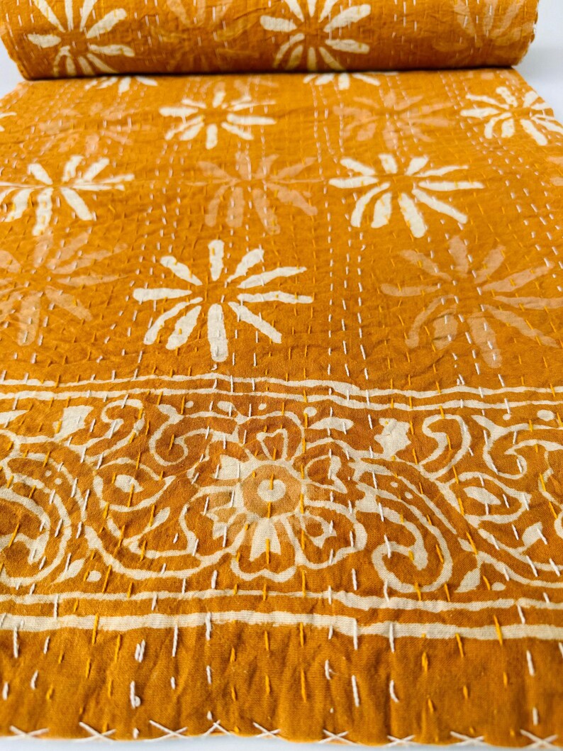 May include: A mustard yellow kantha quilt with a white floral pattern. The quilt has a border with a white paisley design.