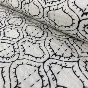 May include: A white fabric featuring a repeating black geometric pattern of interconnected ogee shapes. The textile is detailed with visible black running stitch embroidery that follows the outlines of the printed shapes, creating a textured appearance.