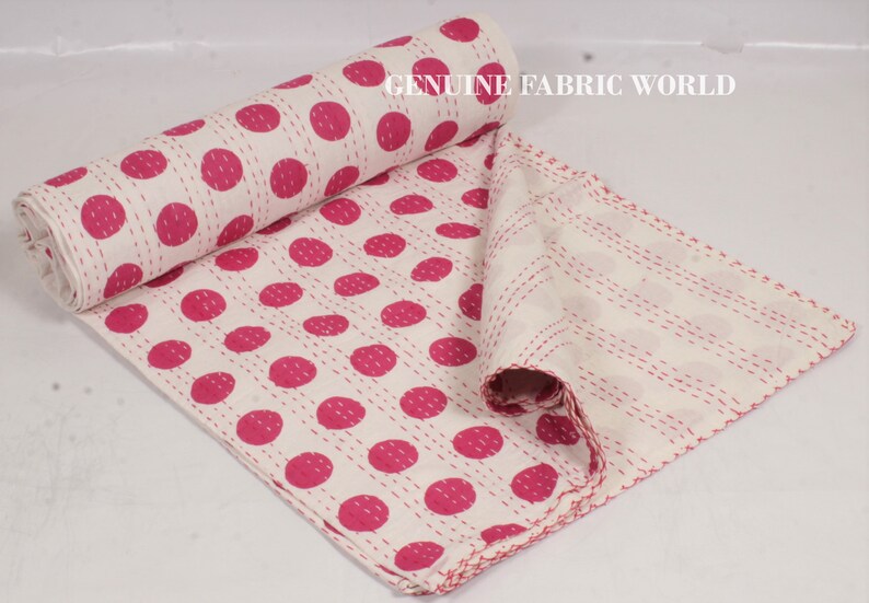 May include: White cotton kantha quilt with pink polka dots. The quilt is folded and rolled up, showing the stitching detail. The text "GENUINE FABRIC WORLD" is visible in the top right corner of the image.