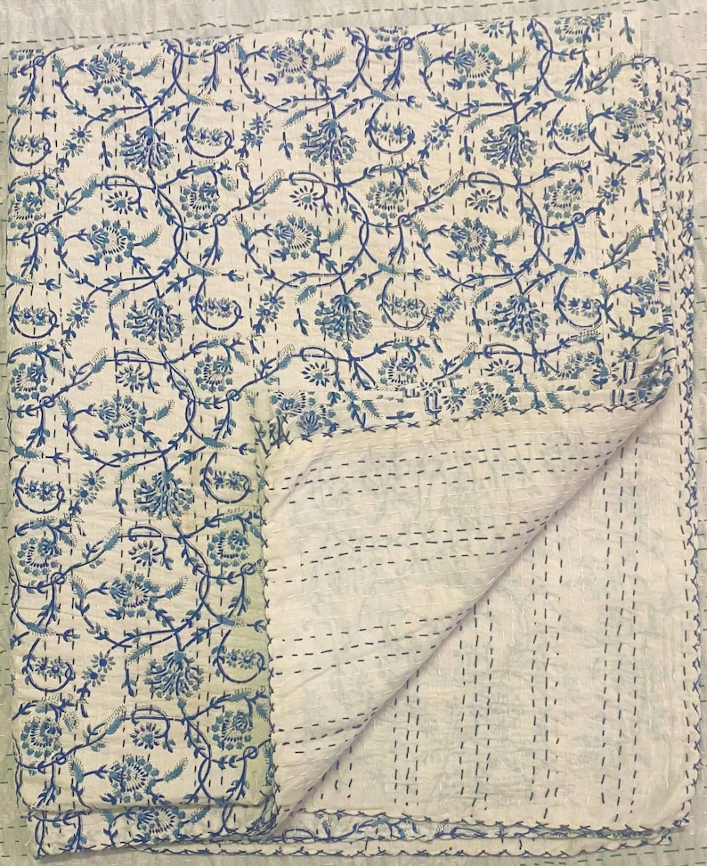 Pode incluir: Uma colcha kantha de algod&atilde;o branco com um padr&atilde;o floral azul. A colcha est&aacute; dobrada ao meio e as costuras s&atilde;o vis&iacute;veis.