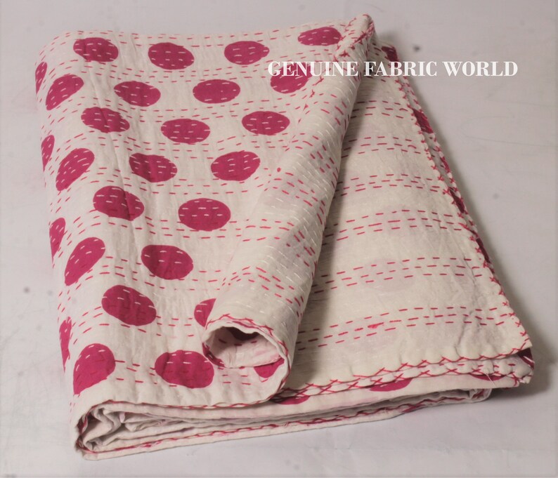 May include: White cotton quilt with a pink polka dot pattern and white stitching. The quilt is folded in half and has a "GENUINE FABRIC WORLD" label in the top right corner.