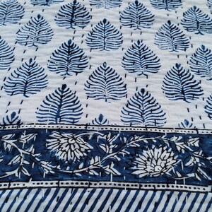 Puede incluir: Una tela de algod&oacute;n blanca con un patr&oacute;n de hojas azules y un borde floral azul. La tela est&aacute; acolchada y tiene una textura suave.