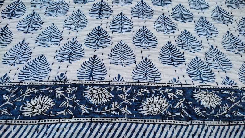 Puede incluir: Una tela de algod&oacute;n blanca con un patr&oacute;n de hojas azules y un borde floral azul. La tela est&aacute; acolchada y tiene una textura suave.