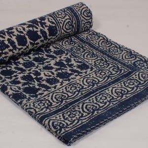 May include: A folded quilt featuring a dark navy blue and off-white floral block print pattern. The textile displays a repeating botanical motif across the centre and a distinct border design with stylised heart and flower shapes throughout.