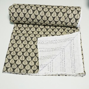 May include: A rolled-up, dark brown and cream-colored quilt with a repeating leaf pattern. The quilt is partially unfolded, revealing a white interior with black stitching. The quilt is made of soft material.