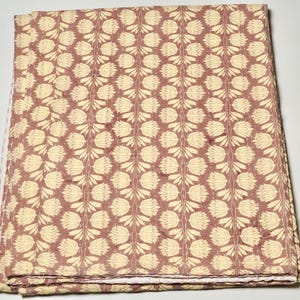 Op de afbeelding: Een rechthoekige quilt met een herhalend verticaal patroon van crèmekleurige gestileerde tulpbloemen op een gedempte mauve achtergrond. De stof vertoont zichtbare doorstiklijnen die verticaal over het gehele oppervlak lopen.