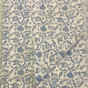 Pode incluir: Uma colcha de algod&atilde;o branco com um padr&atilde;o floral azul. A colcha est&aacute; dobrada ao meio e tem um design acolchoado.