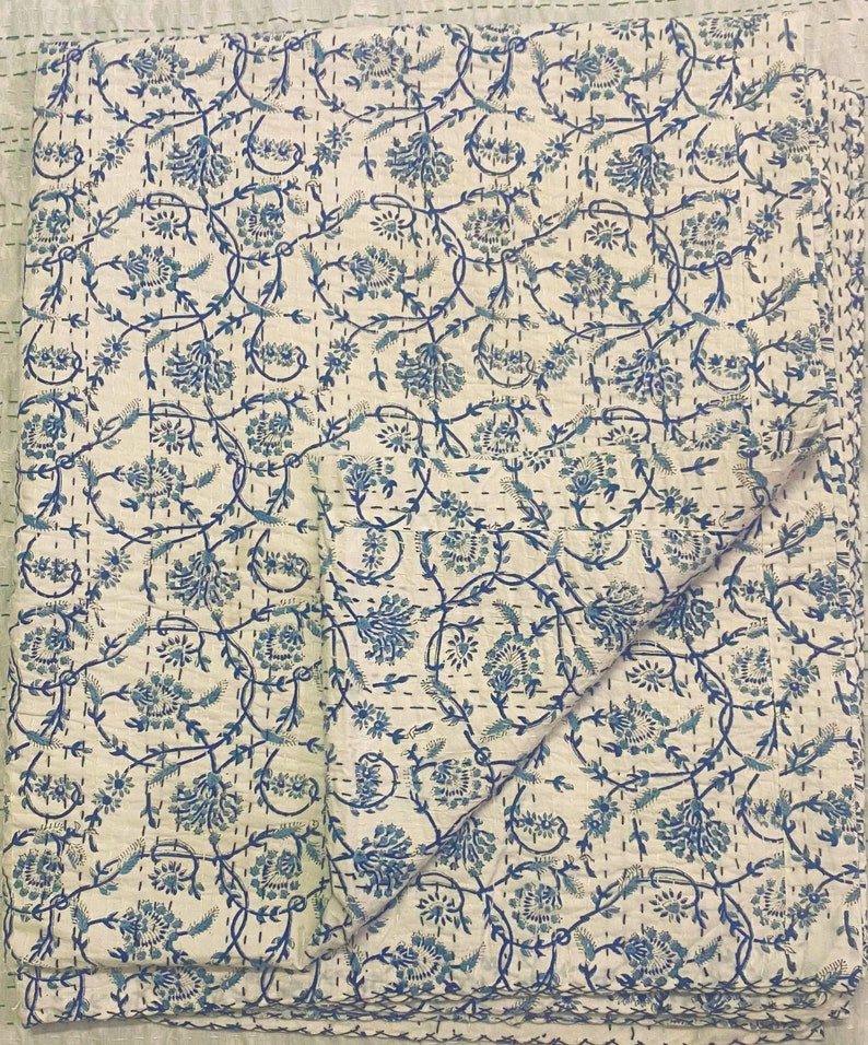 Pode incluir: Uma colcha de algod&atilde;o branco com um padr&atilde;o floral azul. A colcha est&aacute; dobrada ao meio e tem um design acolchoado.