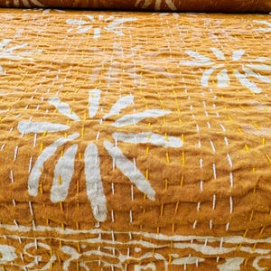 May include: A mustard yellow kantha quilt with a white floral pattern. The quilt is made of cotton and has a hand-stitched design.