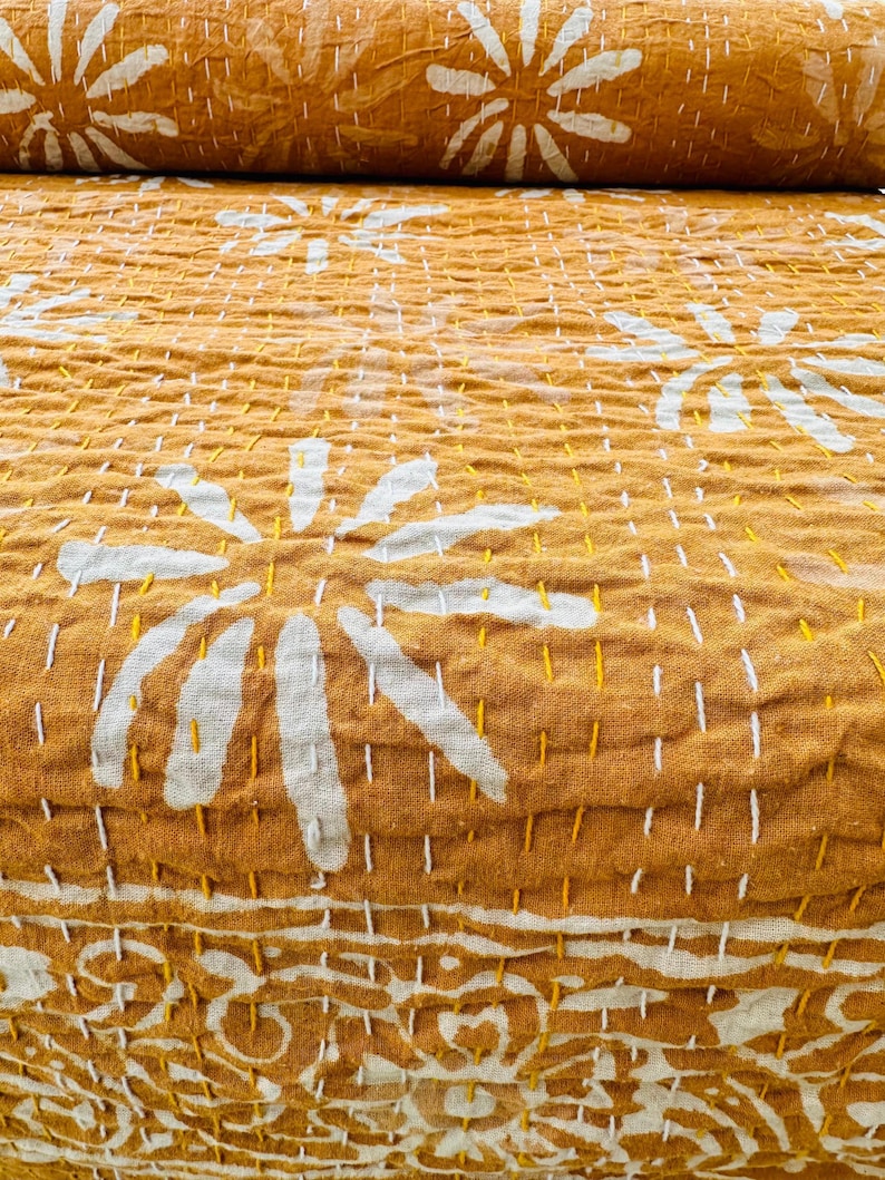 May include: A mustard yellow kantha quilt with a white floral pattern. The quilt is made of cotton and has a hand-stitched design.