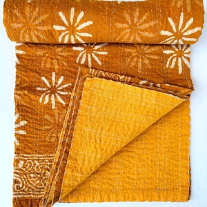 May include: A mustard yellow kantha quilt with a white floral pattern. The quilt is folded in half and the fabric is soft and textured.