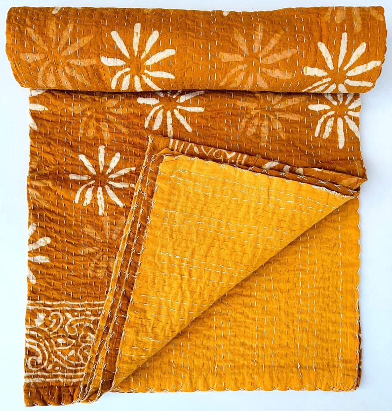 May include: A mustard yellow kantha quilt with a white floral pattern. The quilt is folded in half and the fabric is soft and textured.