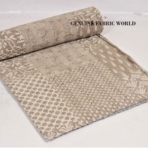 May include: A rolled-up, beige and white patterned quilt with various designs, including floral and geometric patterns. The quilt is made of fabric and has a stitched texture. The text "GENUINE FABRIC WORLD" is visible on the quilt.