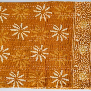 May include: A mustard yellow kantha quilt with a white floral pattern. The quilt has a decorative border with a paisley design.