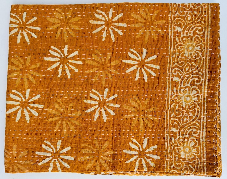 May include: A mustard yellow kantha quilt with a white floral pattern. The quilt has a decorative border with a paisley design.