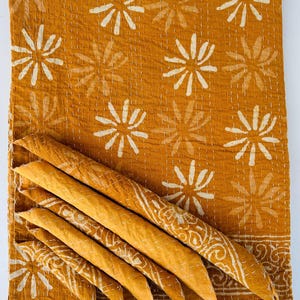 May include: A mustard yellow kantha quilt with a white floral pattern. The quilt is folded in thirds and the fabric is soft and textured.