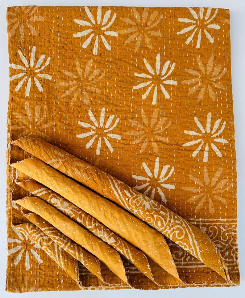 May include: A mustard yellow kantha quilt with a white floral pattern. The quilt is folded in thirds and the fabric is soft and textured.