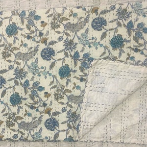 May include: A white cotton quilt with a blue and brown floral pattern. The quilt is folded in half and the stitching is visible.