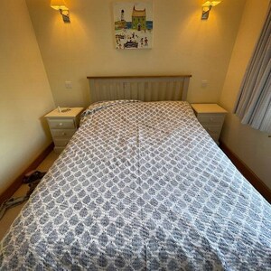 Puede incluir: Una cama blanca con un edred&oacute;n estampado en azul y blanco. La cama est&aacute; en un dormitorio con dos mesitas de noche y un cuadro en la pared.