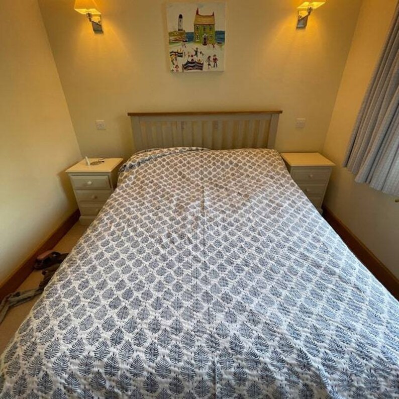 Puede incluir: Una cama blanca con un edred&oacute;n estampado en azul y blanco. La cama est&aacute; en un dormitorio con dos mesitas de noche y un cuadro en la pared.