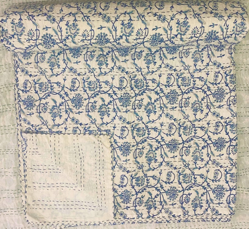 Pode incluir: Uma colcha de algod&atilde;o branco com um padr&atilde;o floral azul. A colcha est&aacute; dobrada ao meio e o padr&atilde;o &eacute; vis&iacute;vel em ambos os lados.