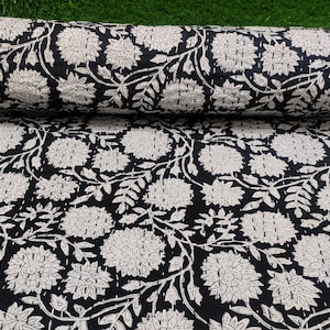 Puede incluir: Edredón enrollado con un diseño floral en blanco y negro. El patrón presenta grandes flores y hojas estilizadas en blanco sobre un fondo negro. La tela está doblada, revelando el patrón en el interior. Ideal para la decoración del hogar.