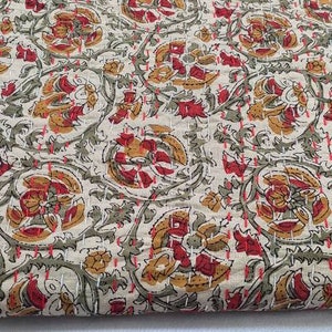May include: A cream-colored fabric with a repeating floral pattern in shades of red, brown, and green. The fabric has a textured surface and a subtle sheen.
