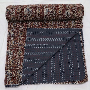 Könnte beinhalten: Eine Kantha-Steppdecke mit einem floralen Muster in Braun-, Creme- und Blautönen. Die Decke ist in der Hälfte gefaltet und zeigt eine dunkelblaue Unterseite mit weißen Nähten.