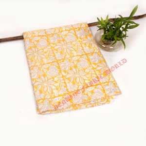 Puede incluir: Tela amarilla con un patrón floral blanco. La tela está doblada y tiene un borde deshilachado. La tela está sobre un fondo blanco.