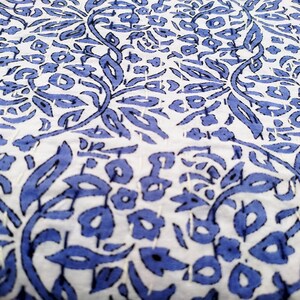May include: White fabric with a blue floral pattern. The pattern is made up of leaves and flowers. The fabric is quilted with white thread.
