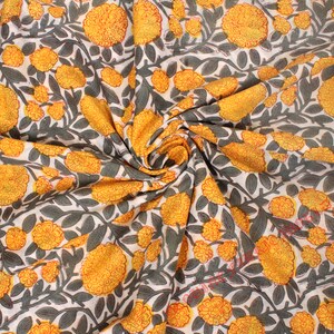 Può includere: Tessuto floreale con un motivo ripetuto di fiori gialli simili a calendule e foglie grigio-verdi su sfondo bianco. Il tessuto è piegato, mostrando la trama e la drappeggiatura del materiale. Il design ricorda una stampa botanica.