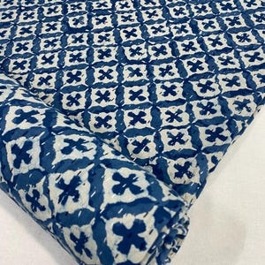 Puede incluir: Una tela de colcha kantha azul y blanca con un patrón geométrico. La tela está doblada y enrollada.
